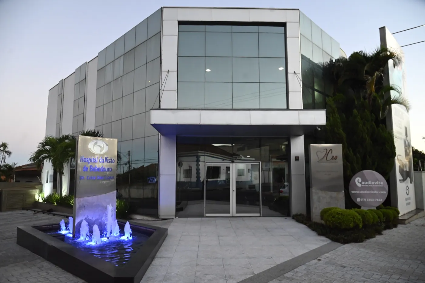 Entrada do Hospital da Visão de Bebedouro vista da rua, com totem de identificação e fonte iluminada